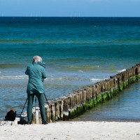 Mann steht am Meeresufer und fotografiert