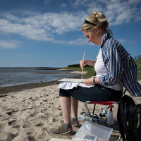 Frau sitzt am Ufer und malt